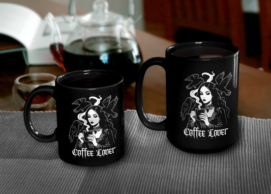 Two different sized black mugs with gothic 'Coffee Lover' design on a table with a teapot in the background.