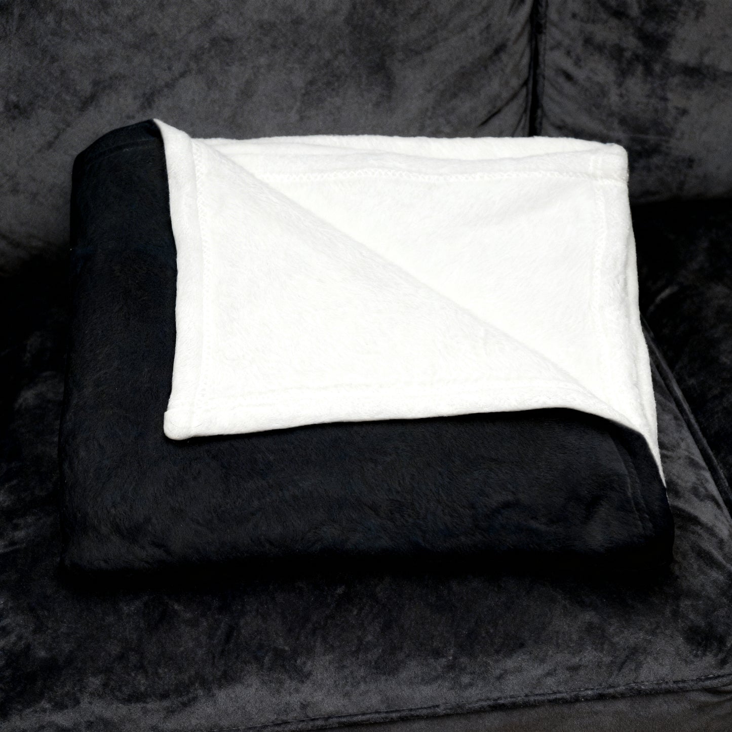 Folded dark velveteen blanket with white plush underside folded on a black velvet sofa