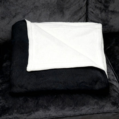 Folded dark velveteen blanket with white plush underside folded on a black velvet sofa